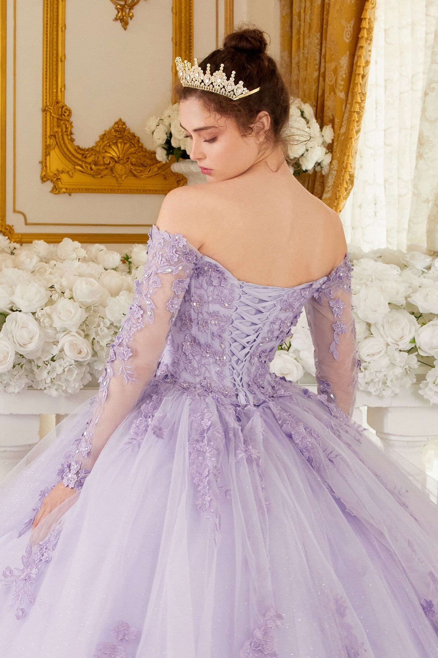 This gorgeous lilac off-the-shoulder, long-sleeved ball gown is an enchanting piece of work that will make you look like a quinceanera princess! The crafted lace and beaded applique add the perfect amount of shine to the bodice. Adding to the charm of this dress are the dimensional floral appliques giving it a unique and creative flair